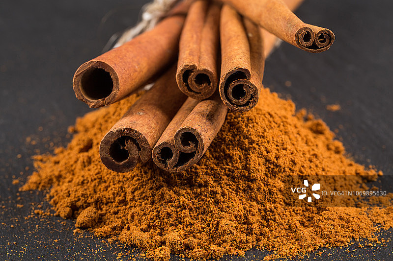 深色石板上的肉桂棒与粉末图片素材