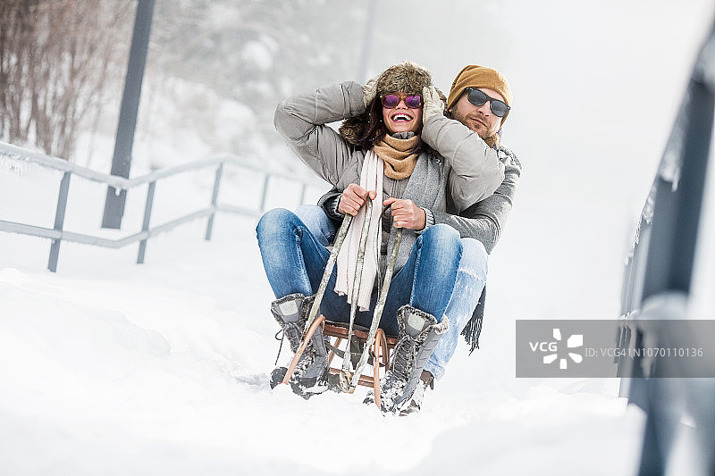 年轻情侣在雪地里玩雪橇图片素材