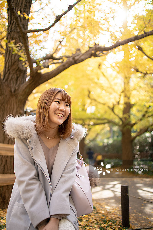 秋天银杏树下微笑的年轻女人图片素材