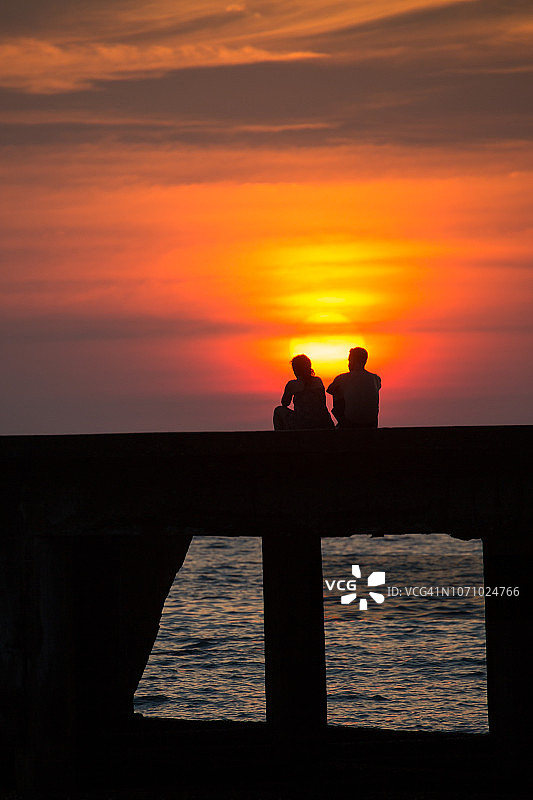 阁骨岛：一对旅行者坐在码头上欣赏日落图片素材