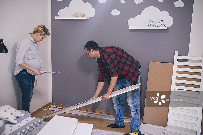 幸福夫妇在家期待宝宝出生，男人正在修理婴儿床。图片素材