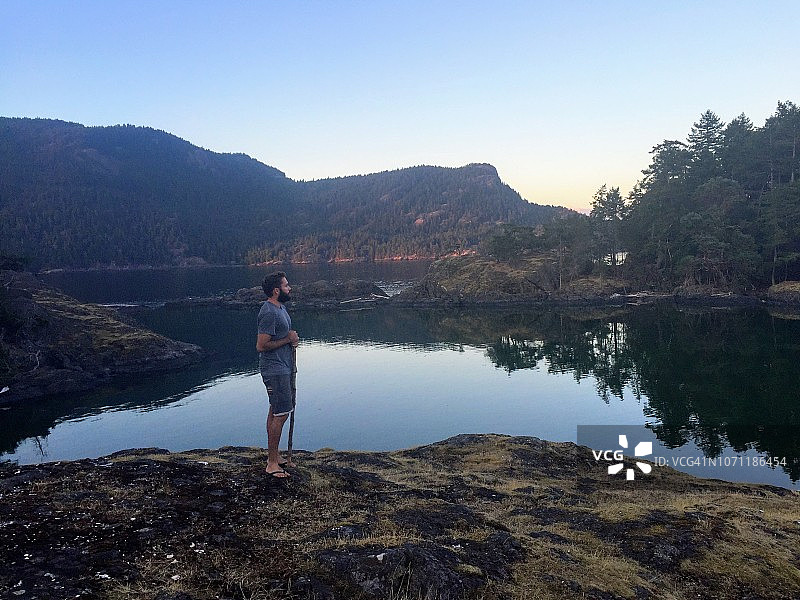 夕阳西下，一名男子站在加拿大不列颠哥伦比亚省海湾群岛的岸边沉思图片素材