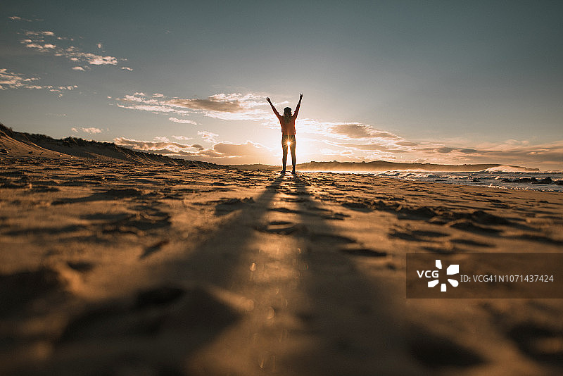日落时举起双臂的年轻女人图片素材