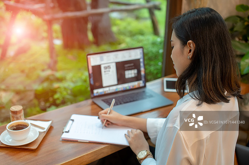 亚洲女性在咖啡馆思考并用笔在笔记本上写作图片素材