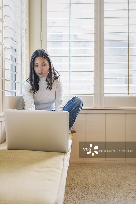 年轻女人在家中穿着毛衣使用笔记本电脑图片素材