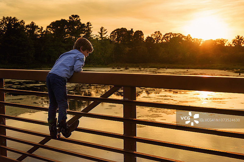 日落时分在美国攀爬桥梁栏杆的男孩图片素材
