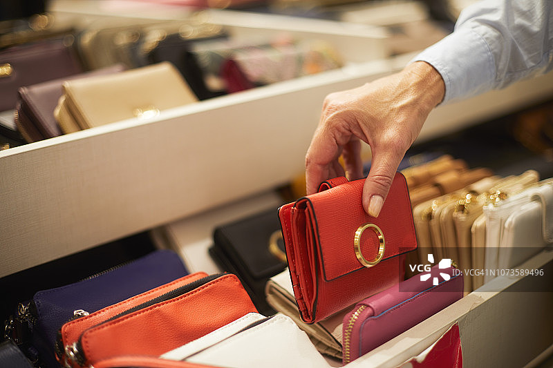 在箱包店货架上挑选红色钱包的年长女士图片素材