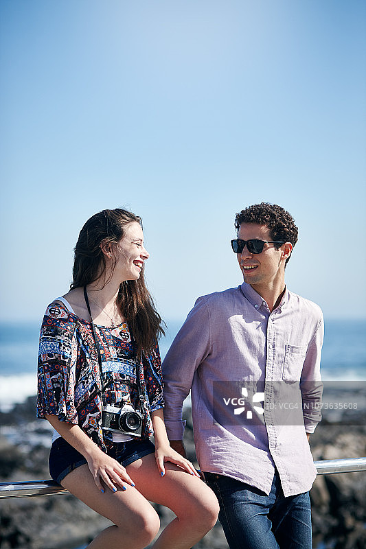 微笑的年轻情侣坐在海边的栅栏上度假图片素材