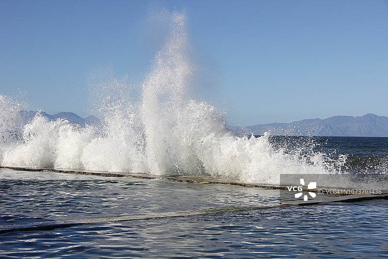 南非西开普省开普敦附近，福尔斯湾海岸的潮汐游泳池的墙壁上，白色泡沫浪花拍打着图片素材