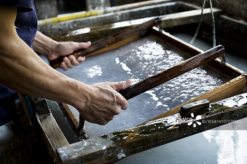 日本男人在工作室制作传统和纸，手持带压制纸浆的木框图片素材