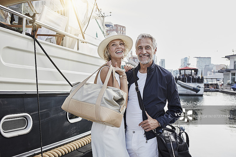 年长的男人和年轻的女人带着旅行包站在游艇旁的码头上图片素材