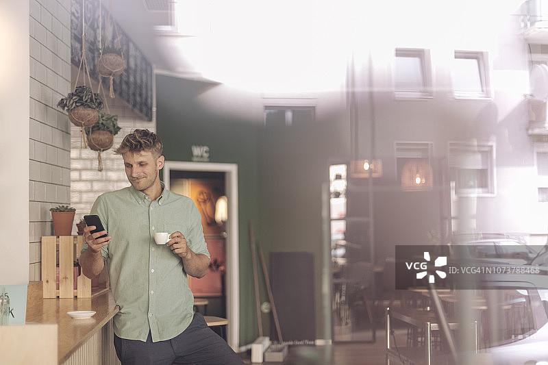 年轻的店主喝着咖啡，查看智能手机图片素材
