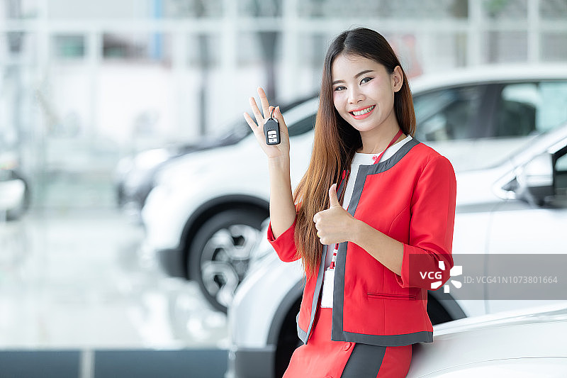 亚洲女销售在车展背景前递交车钥匙，汽车销售业务场景图片素材