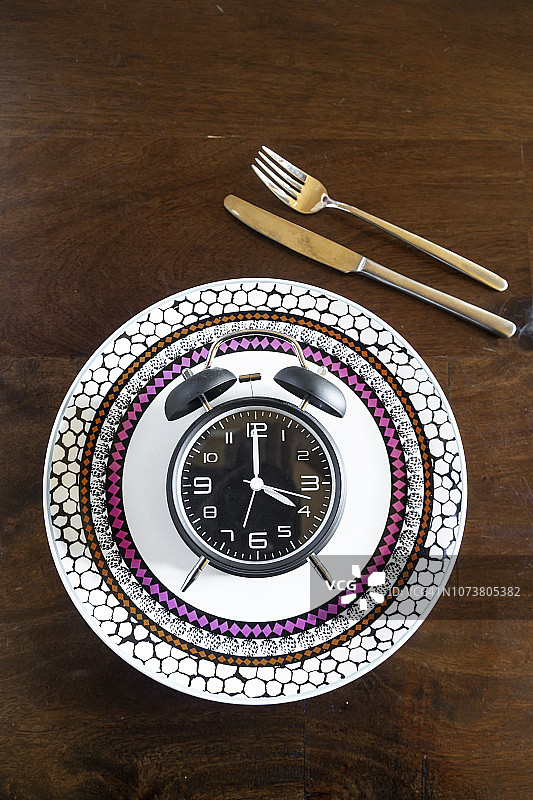 间歇性禁食：16:8禁食，闹钟放在盘子上图片素材