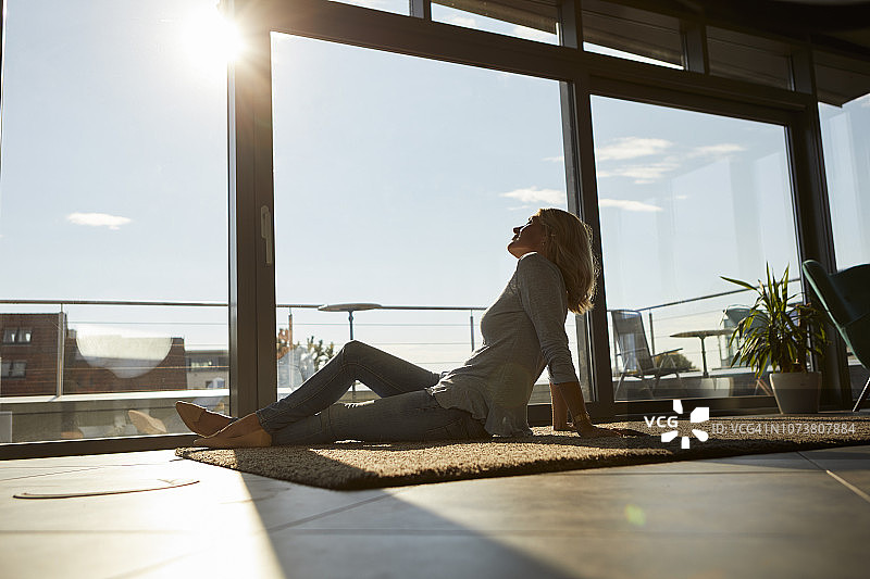 在家中阳光下坐在地毯上放松的中年妇女图片素材