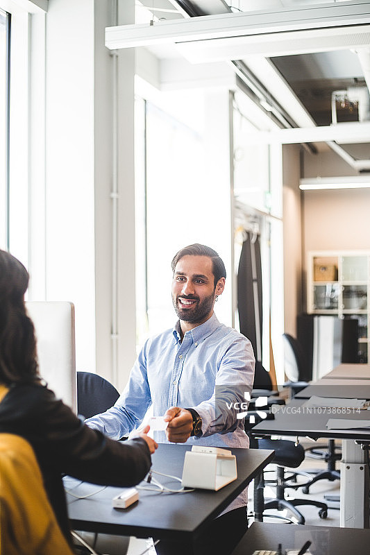 在办公室柜台向女企业家递名片的微笑商人图片素材