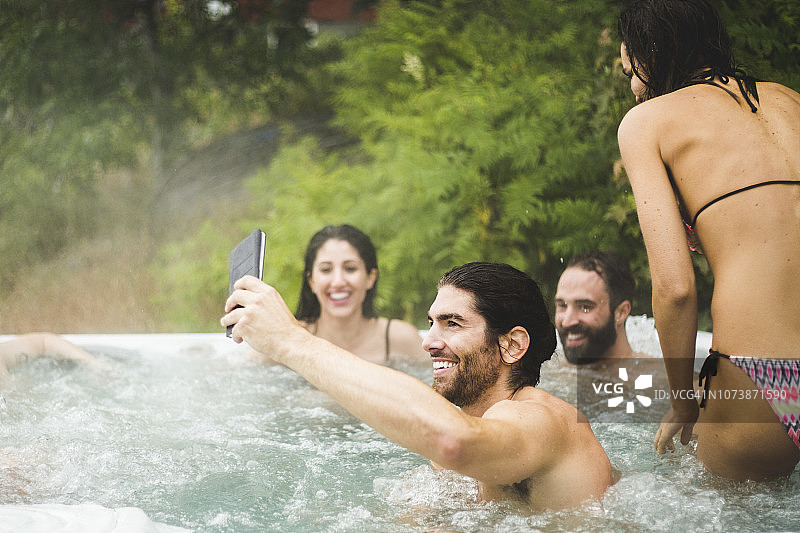年轻男人在朋友们享受周末温泉浴时用手机自拍图片素材