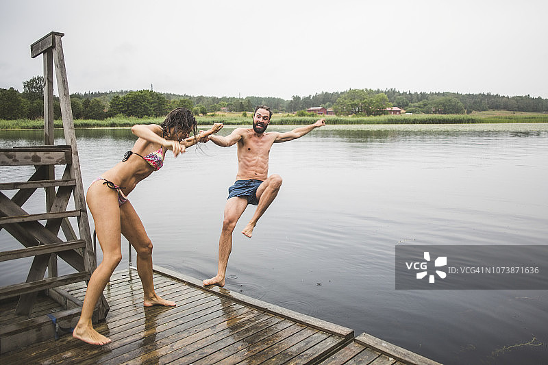 周末度假时，站在码头上推男性朋友的快乐女子全身照图片素材