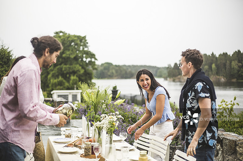 快乐的多民族朋友在后院为晚宴布置餐桌，背景是晴朗的天空图片素材