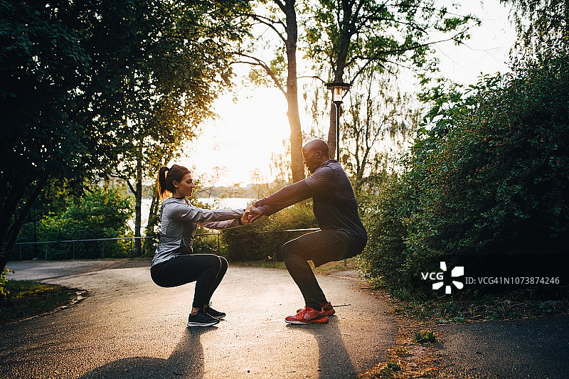 男女运动员在公园道路上练习椅子姿势时手牵着手图片素材