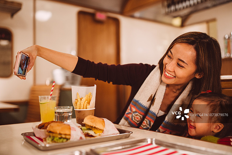 在餐厅里，年轻妈妈和可爱的女儿快乐地自拍图片素材
