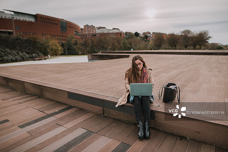 年轻女子坐在公园里用笔记本电脑图片素材