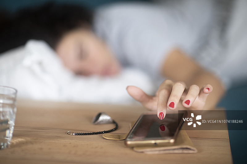 女人在床上关掉手机上的闹钟图片素材