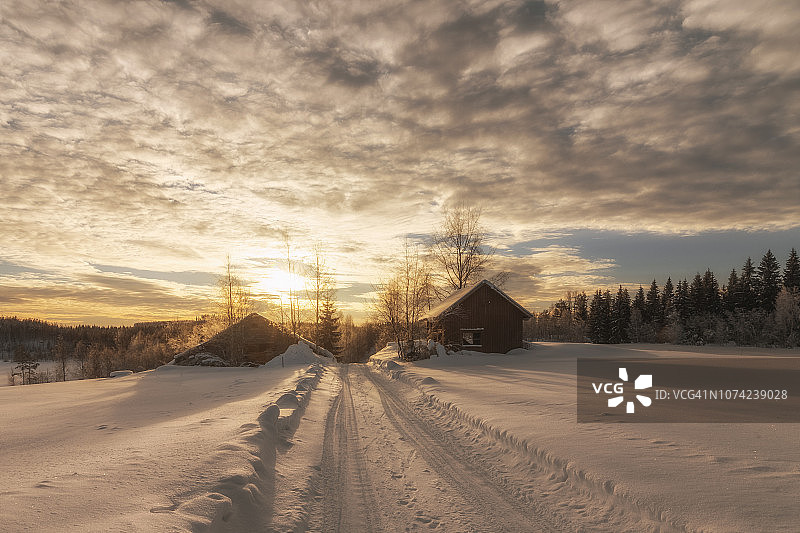 芬兰约恩苏的冬季小路、谷仓和日落云彩图片素材