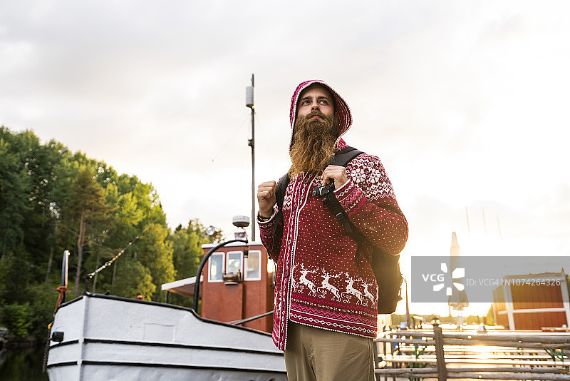 芬兰卡亚尼：身穿连帽夹克、背着背包站在码头上的开朗年轻人图片素材