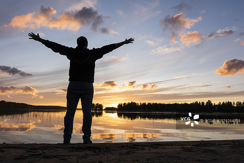 芬兰卡亚尼：男子在河边伸开双臂欣赏日落图片素材