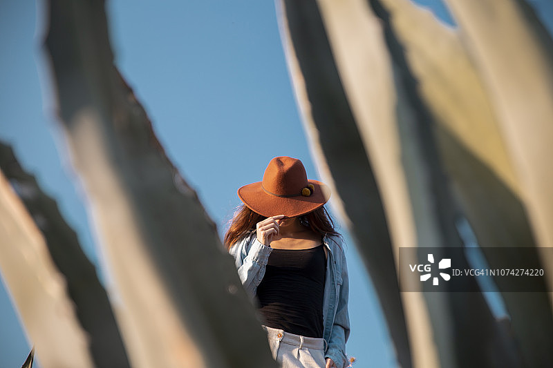 年轻女人戴着帽子站在乡村的龙舌兰后面图片素材