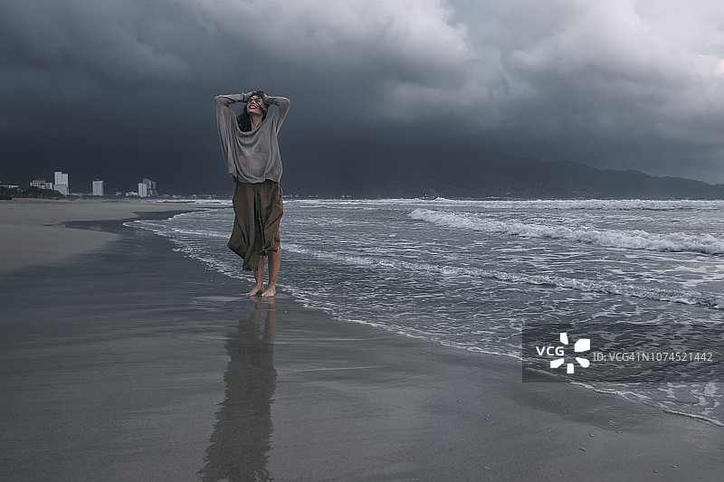 阴雨天在暴风雨海滩上的年轻女人图片素材