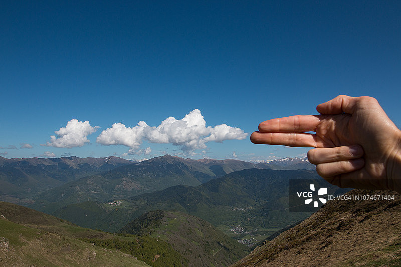 男人的手指像枪一样指着，模拟在山景中用枪射击云彩图片素材