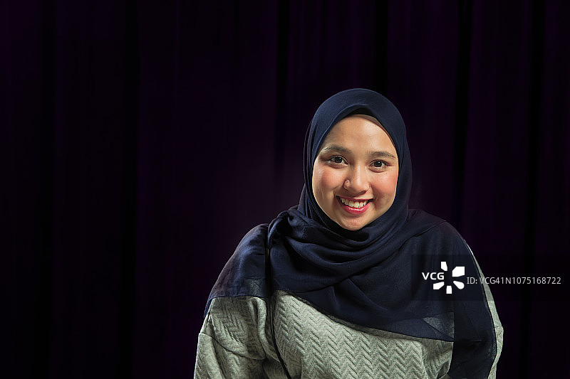在深蓝色背景下微笑的美丽年轻穆斯林女性肖像图片素材