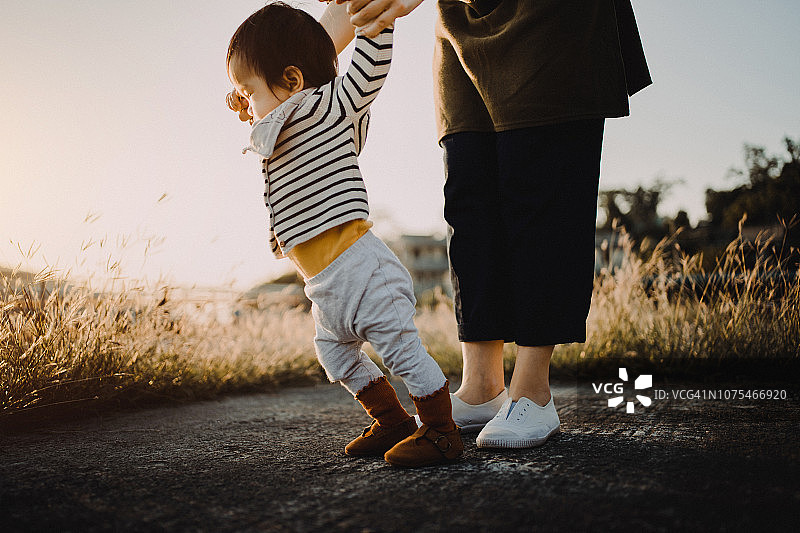 日落时分，母亲牵着女儿的手在公园里学走路图片素材