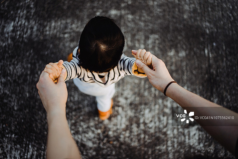 母亲握着女儿的手，帮助她学习走路俯视角度照片图片素材