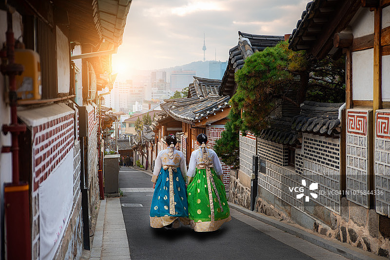两名穿着韩服的女子走在韩国首尔北村韩屋村的传统房屋后面图片素材
