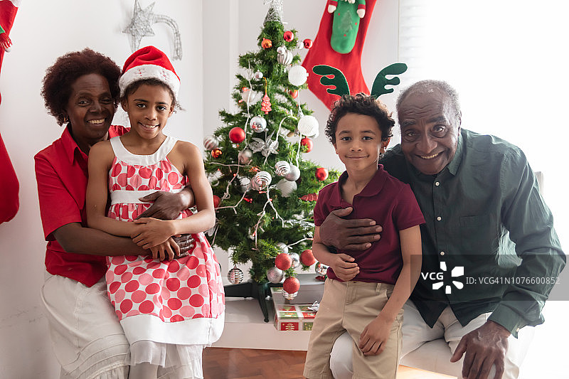坐在祖父母腿上，对着镜头微笑，背景是圣诞装饰品的可爱孙子孙女们图片素材
