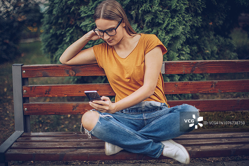 坐在长椅上发短信的年轻女孩图片素材