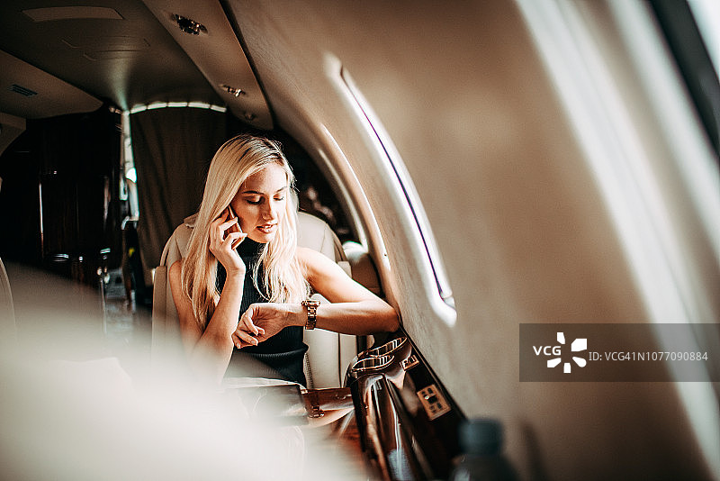时尚金发女商人在私人飞机上查看时间和通话图片素材