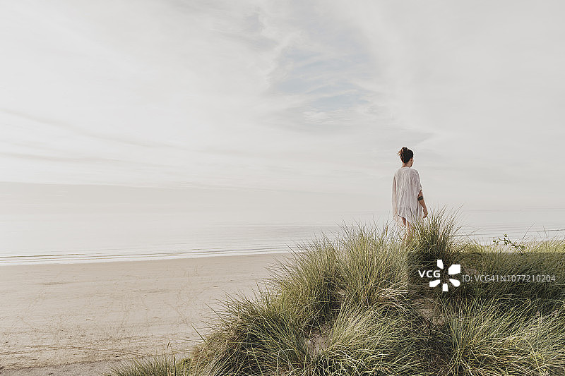站在康沃尔郡Gwithian Towans海滩沙丘顶上享受夏末阳光的女人图片素材