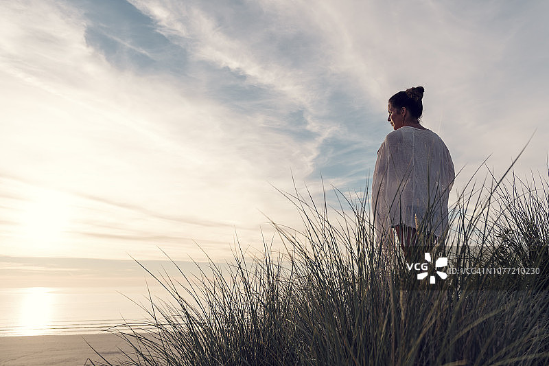 站在康沃尔郡Gwithian Towans海滩沙丘顶上享受夏末阳光的女人图片素材