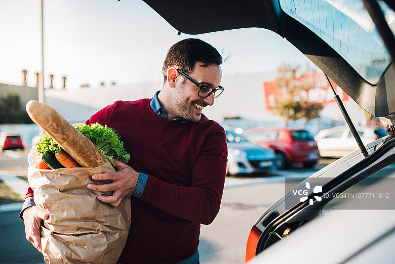 年轻男人将食品杂货放入汽车图片素材
