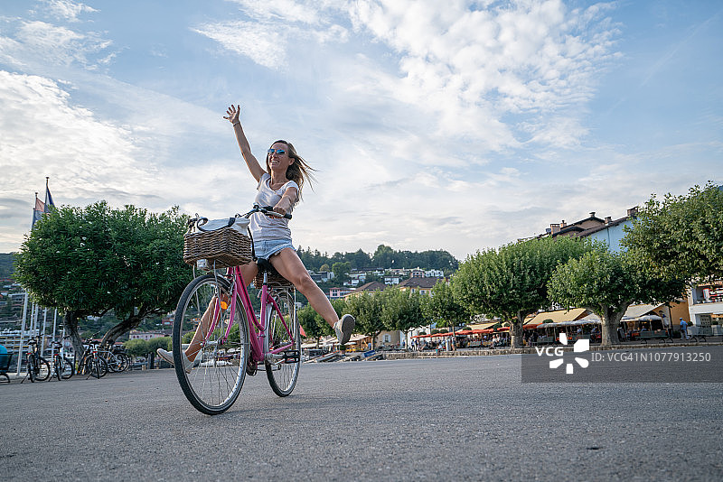 快乐的女人在城市湖边骑自行车，享受夏日自然风光图片素材