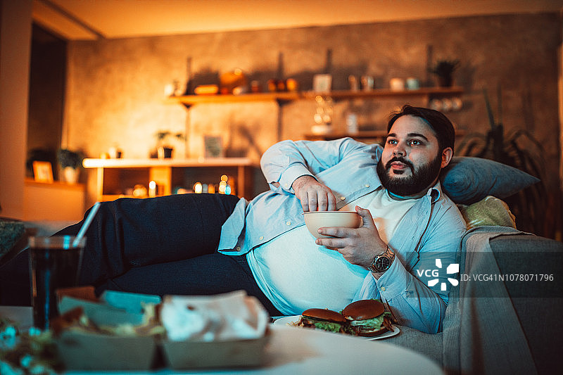 在沙发上吃东西的胖男人图片素材