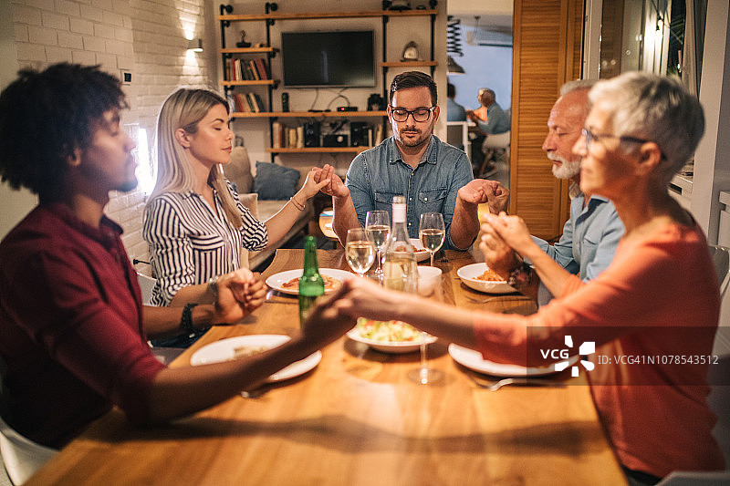 家人和朋友在晚餐前手牵手祈祷图片素材