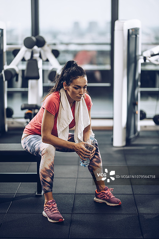 疲惫的汗流浃背的女人在健身房喝水休息图片素材