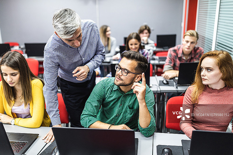 中年教授在电脑室课堂上辅导年轻学生图片素材
