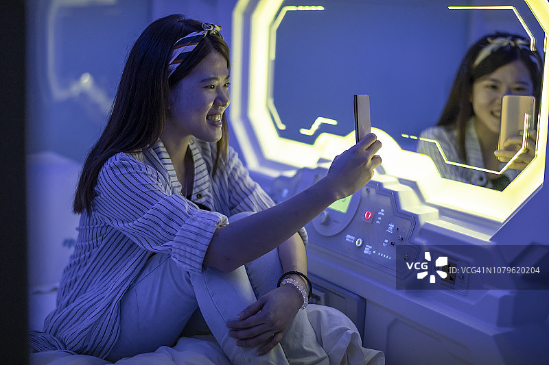 坐在太空舱旅馆床上看手机微笑的中国女性图片素材
