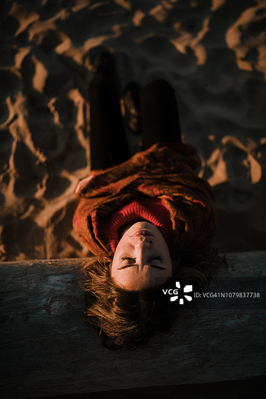 年轻女人坐在冬季日落的海滩边图片素材